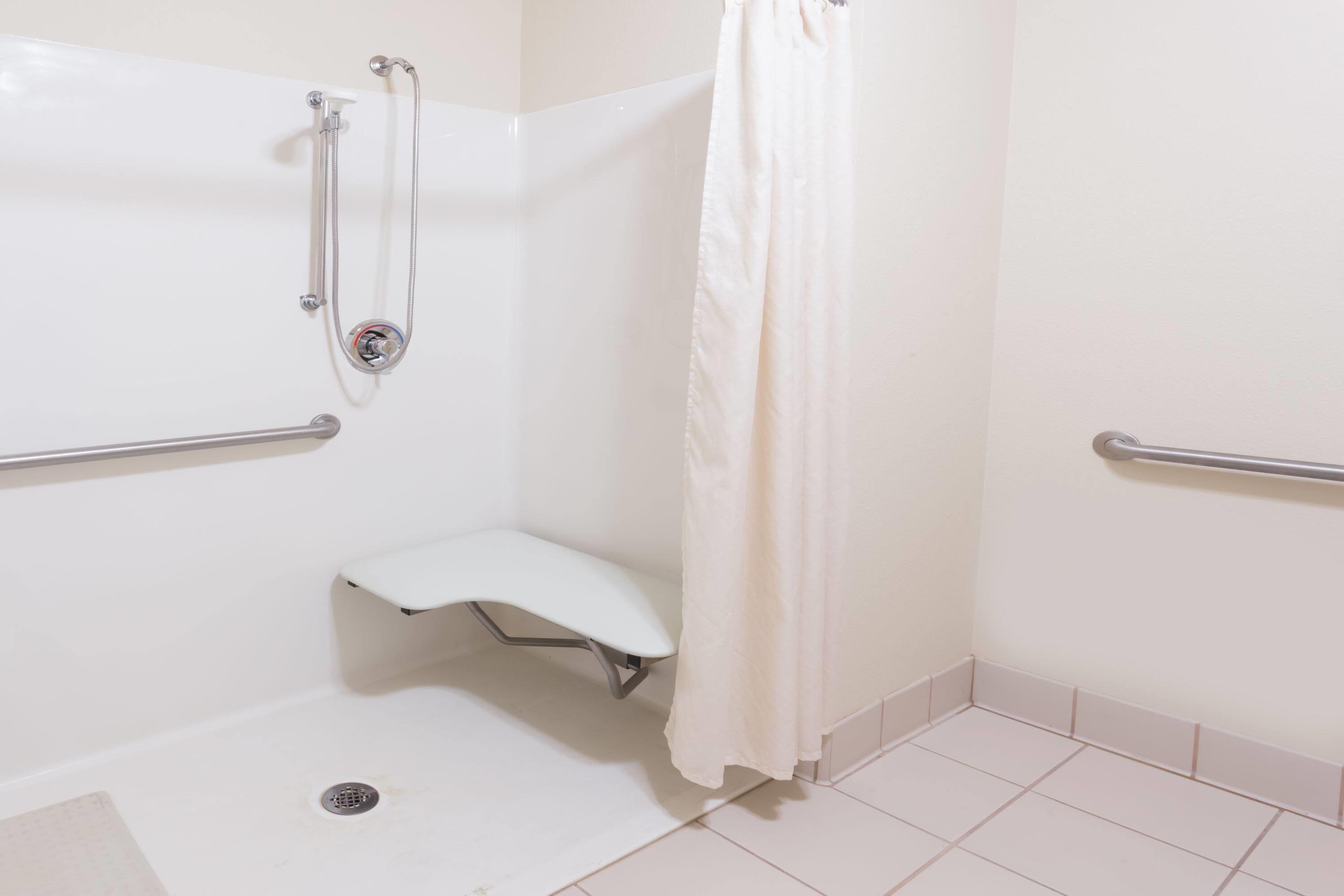 Een witte badkamer met een douche, handgrepen en een witte bank.