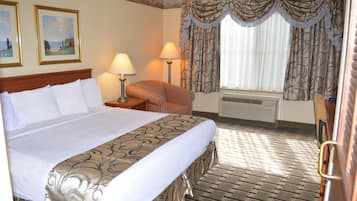 Una habitación de hotel con una cama grande, una silla, un escritorio y una ventana con cortinas.