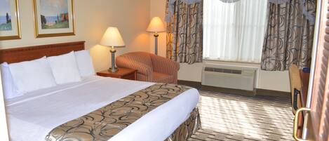 Een hotelkamer met een groot bed, een stoel, een bureau en een raam met gordijnen.