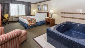 Habitació d'hotel amb un llit, dues làmpades de nit, una banyera gran, un armari amb ratlles i un escriptori amb cadira.