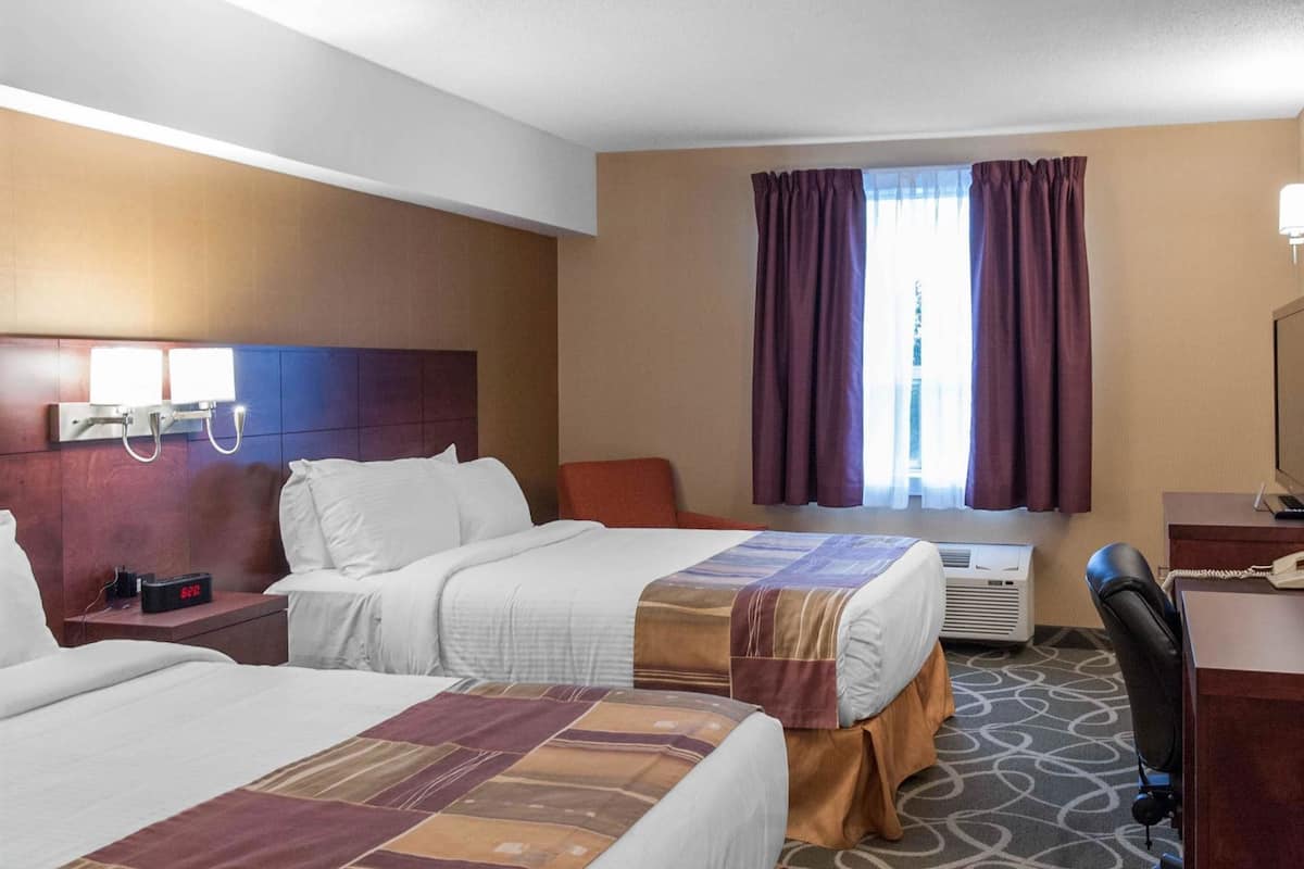 Habitació d'hotel amb dos llits, una taula de nit amb un telèfon, un aparell d'aire condicionat i una finestra amb cortines.