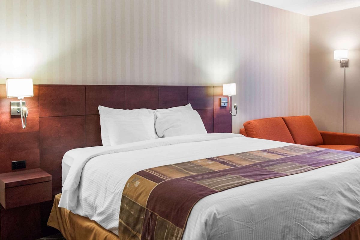 Habitació d'hotel amb un llit gran, una taula de nit, una cadira i dues làmpades penjades a la paret.