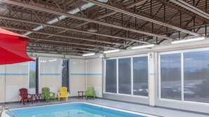 Uma piscina interior com cobertura metálica, janelas amplas e cadeiras Adirondack coloridas.