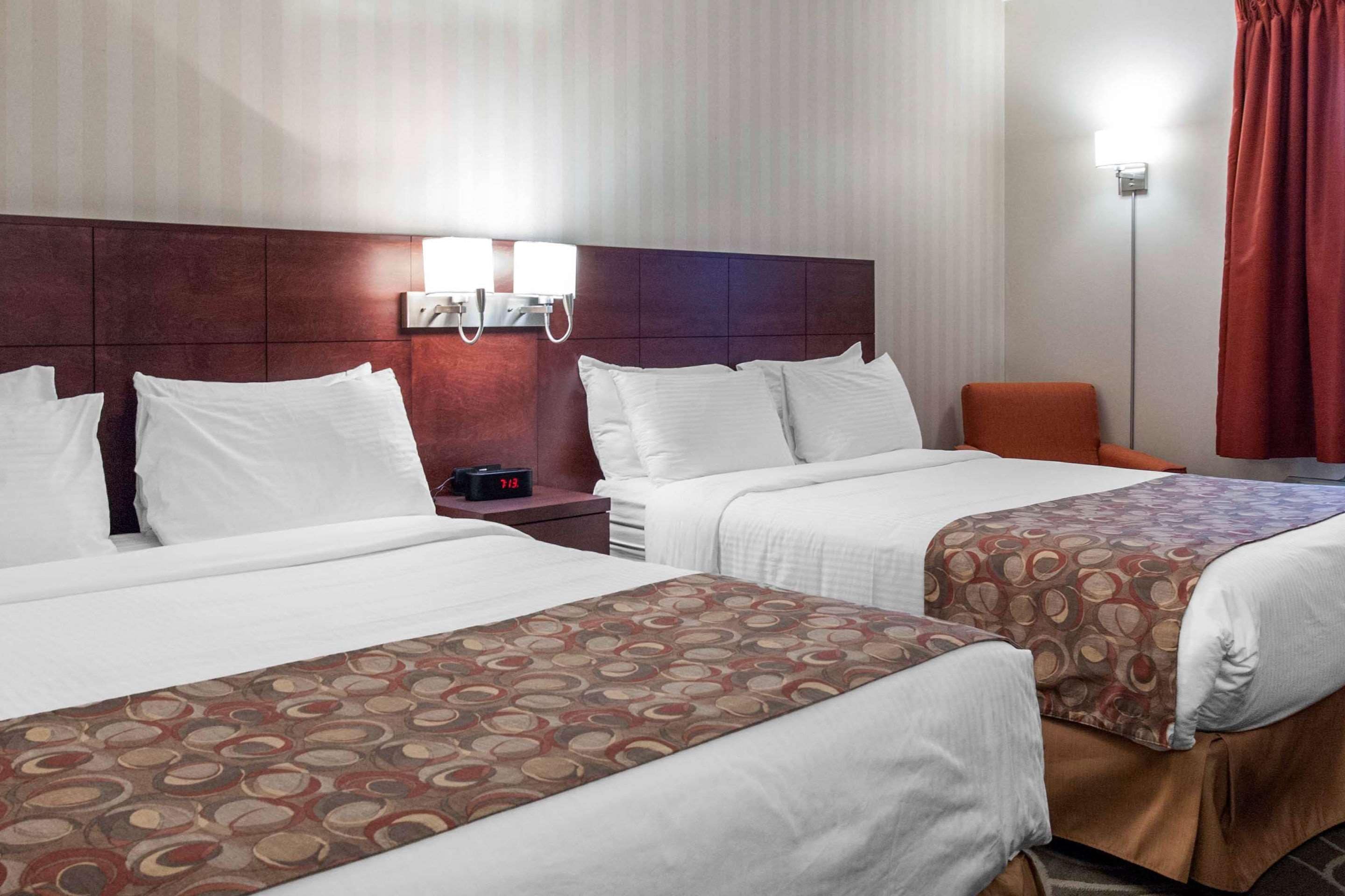 A hotel room with two beds, a nightstand with a clock, and a wall-mounted light fixture.