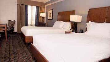 A hotel room with two beds, a desk, a chair, and a lamp.