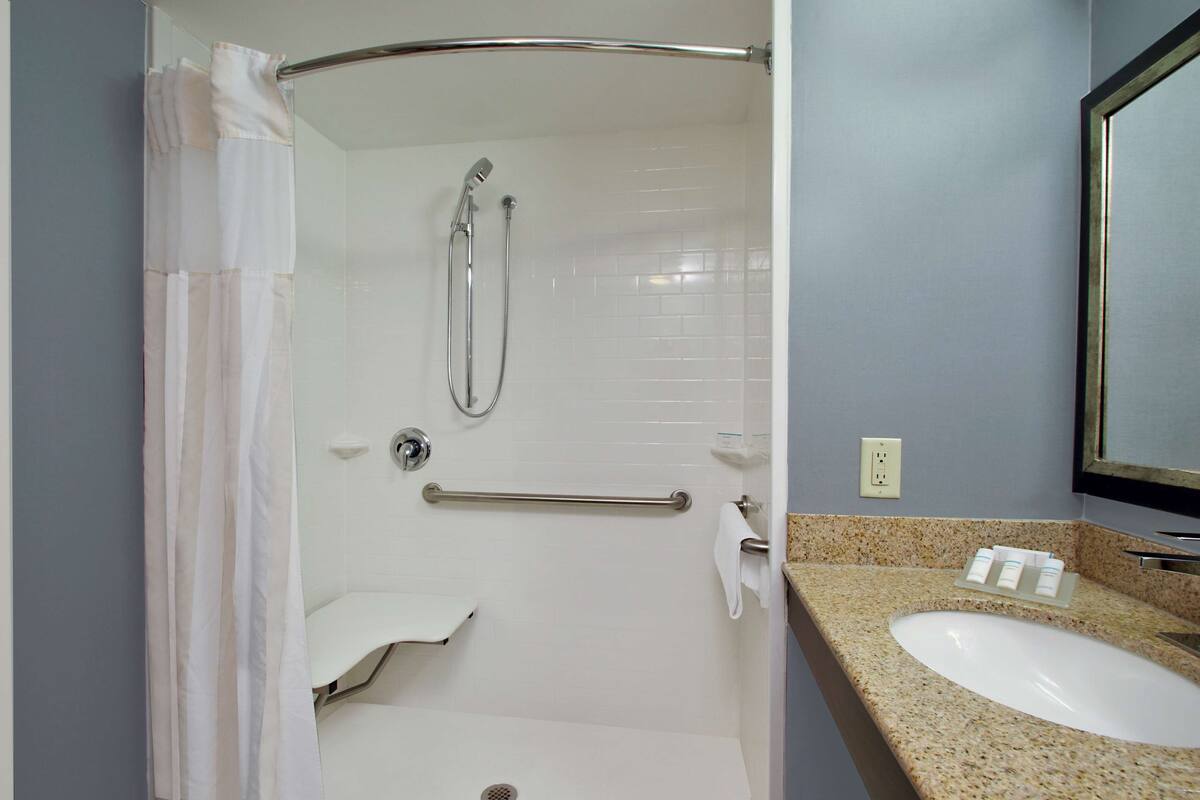 A bathroom with a shower, grab bar, sink, and mirror.