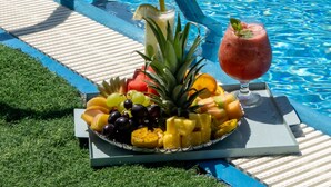 Área da piscina com espreguiçadeiras, um prato de frutas e uma bebida.