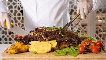 Un chef cortando un plato grande de carne sazonada sobre una tabla de madera, adornado con piñas, tomates y lechuga.