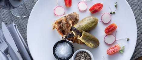 Un plato con pepinillos, tomates, rábanos y un trozo de carne, acompañado de saleros y pimenteros.