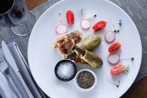 Un plato con pepinillos, tomates, rábanos y un trozo de carne, acompañado de saleros y pimenteros.