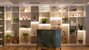 Um interior moderno com piso de madeira, uma mesa consola azul central e prateleiras com objetos decorativos e plantas.