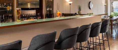 Zona de bar con una barra larga, varios taburetes, una pantalla de televisión y una variedad de botellas y vasos.