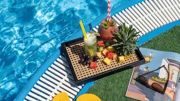 Area piscina con vassoio di bevande, frutta e ciabatte, e una rivista sull'erba.