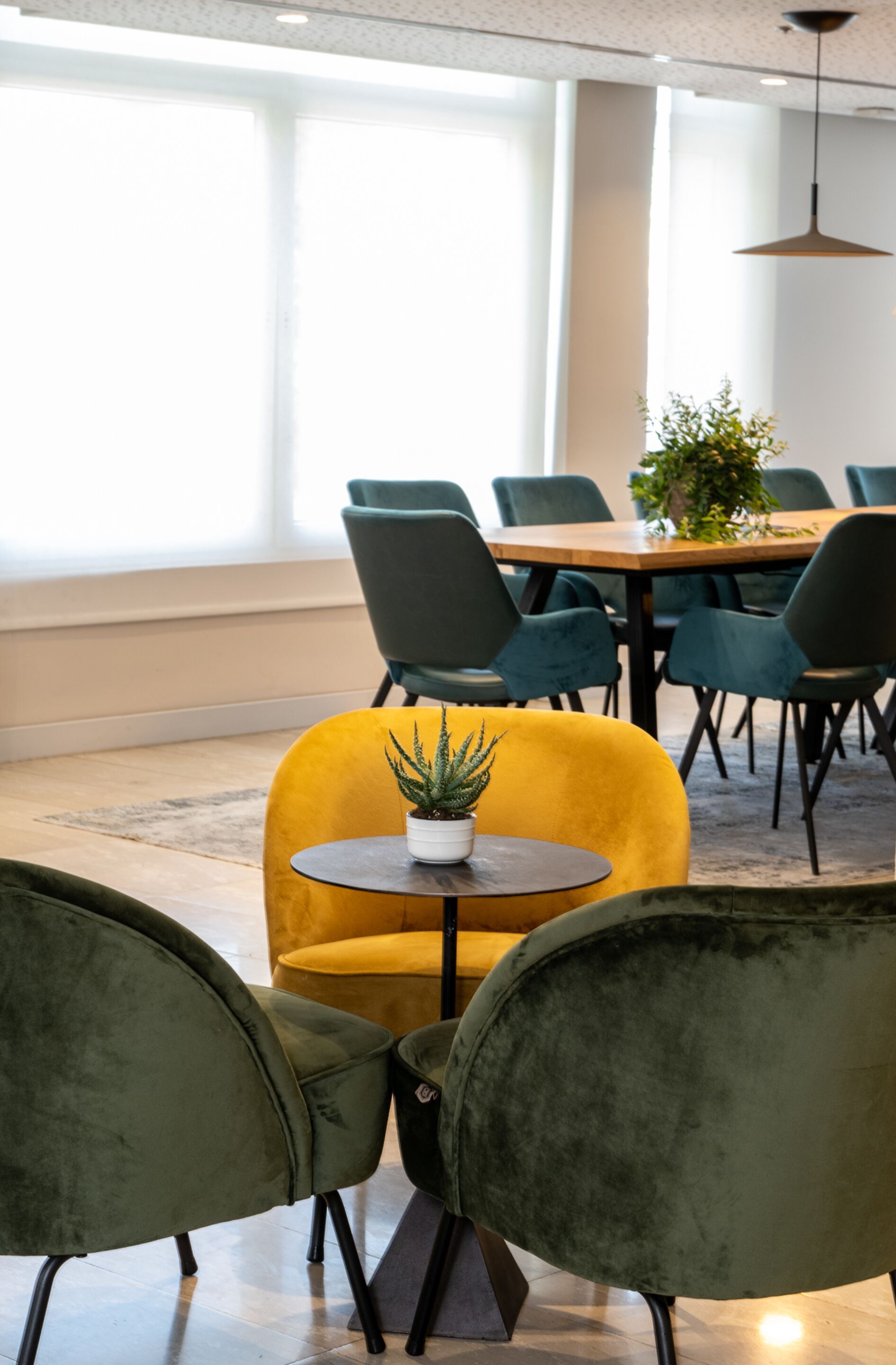 A conference room with a wooden table, green chairs, and a yellow chair with a plant.