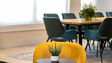 Un salón de conferencias con una mesa de madera, sillas verdes y una silla amarilla con una planta.