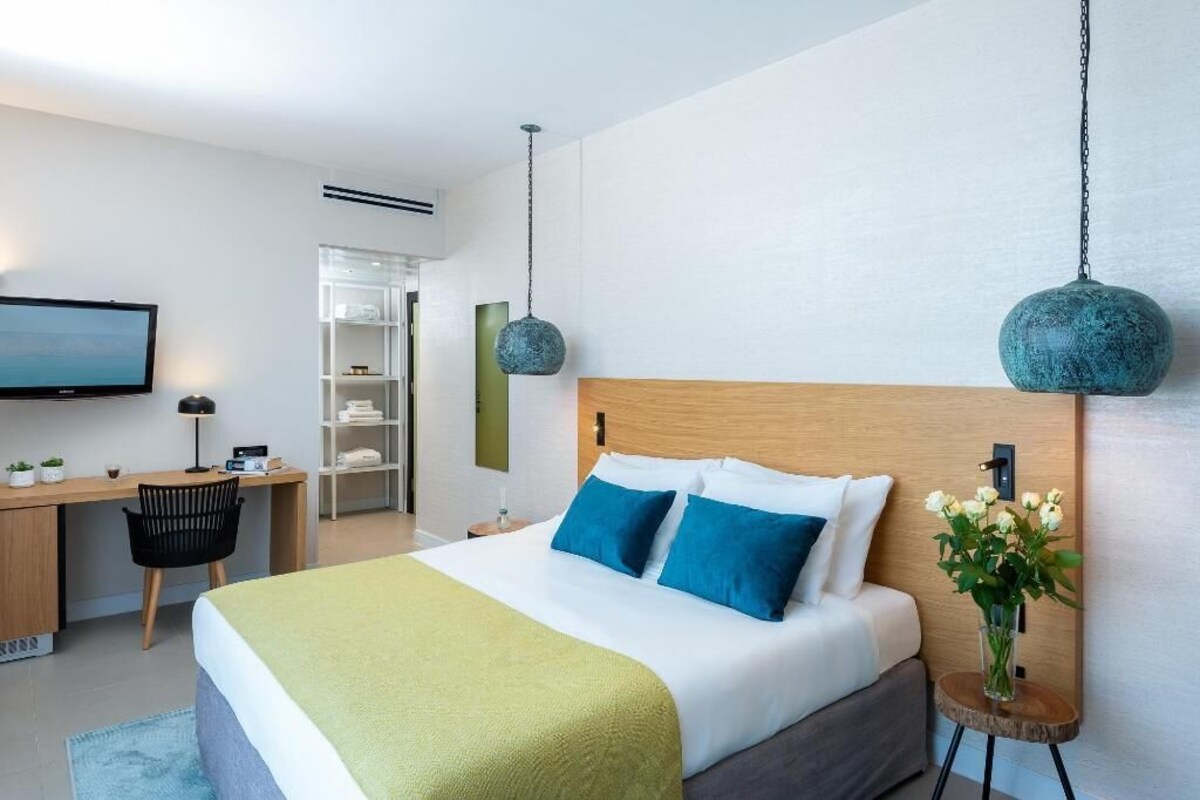 Una habitación de hotel moderna con cama, escritorio, silla, televisor y una mesita de noche con flores.