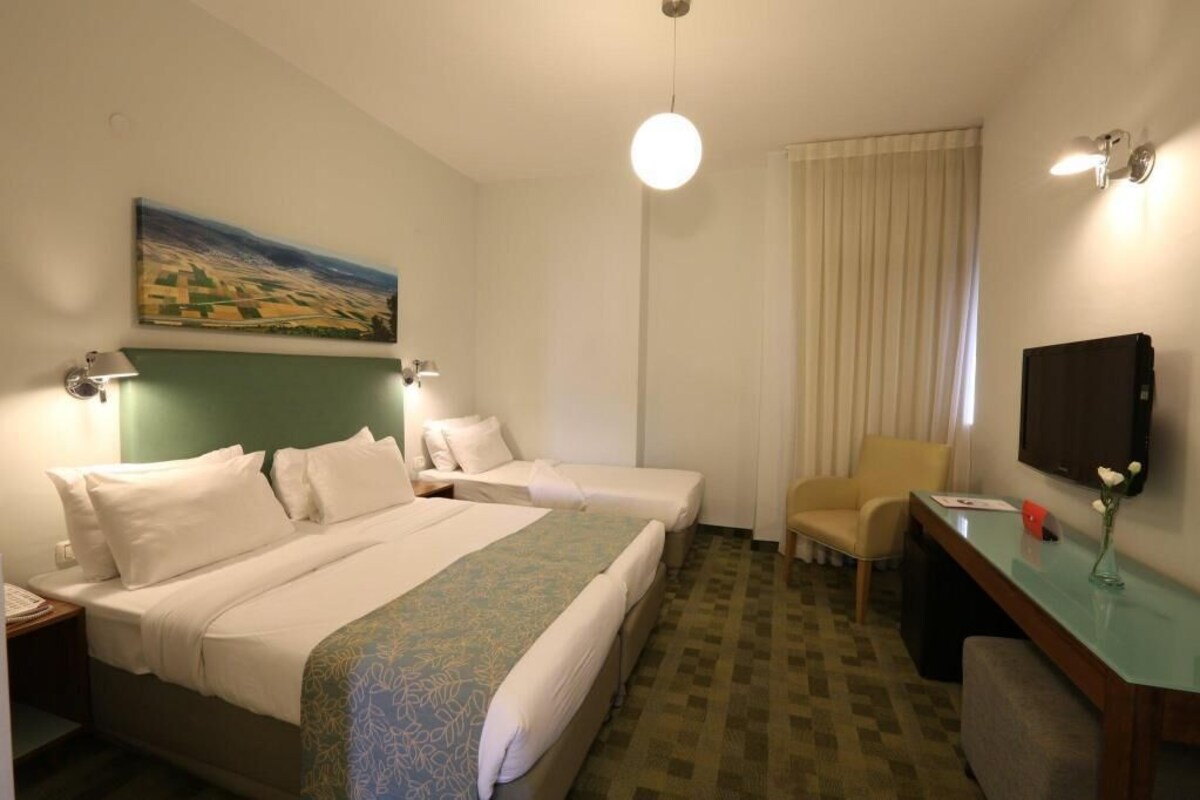 Habitación de hotel con dos camas, un escritorio, una silla, un televisor y un cuadro en la pared.