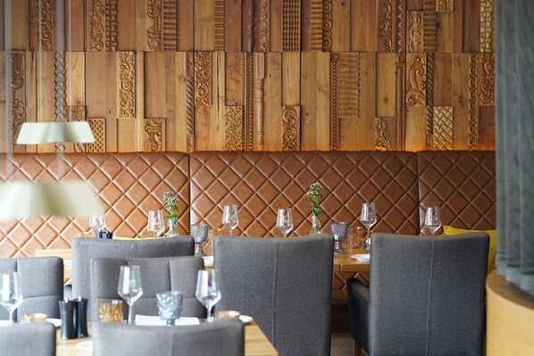 A restaurant with a wooden panel wall, grey upholstered chairs, and tables set with wine glasses and cutlery. - Hotel Am Markt (Nordenham)