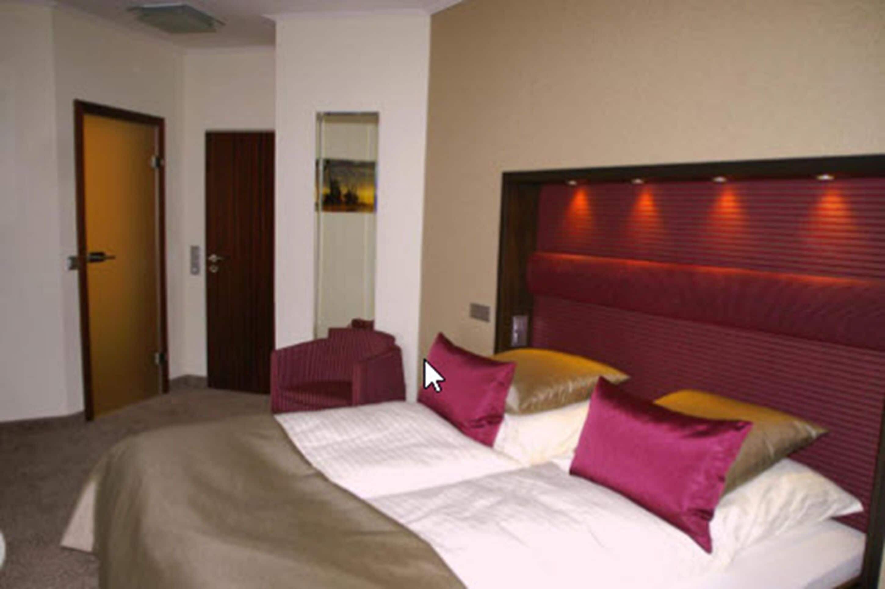 A hotel room with a large bed, a headboard with built-in lighting, a door, and a mirror.