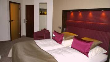 A hotel room with a large bed, a headboard with built-in lighting, a door, and a mirror.