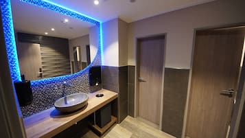 A modern bathroom with a large mirror, a wooden vanity, a stone sink, and a blue LED light strip.