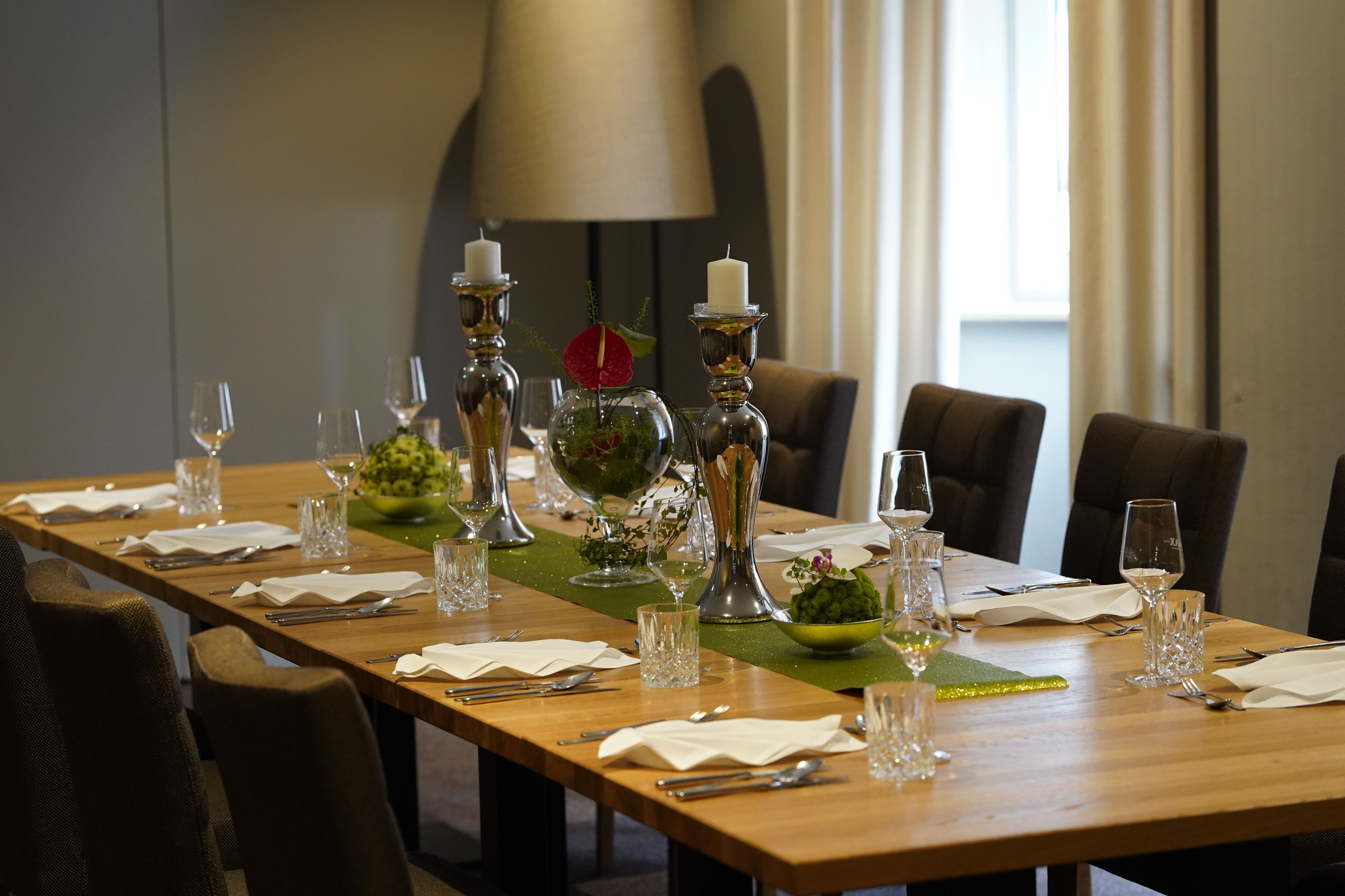 A dining table set for a meal with candles, glassware, and a green centerpiece.