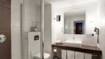 Un baño moderno con cabina de ducha de vidrio, lavabo blanco y un espejo grande.