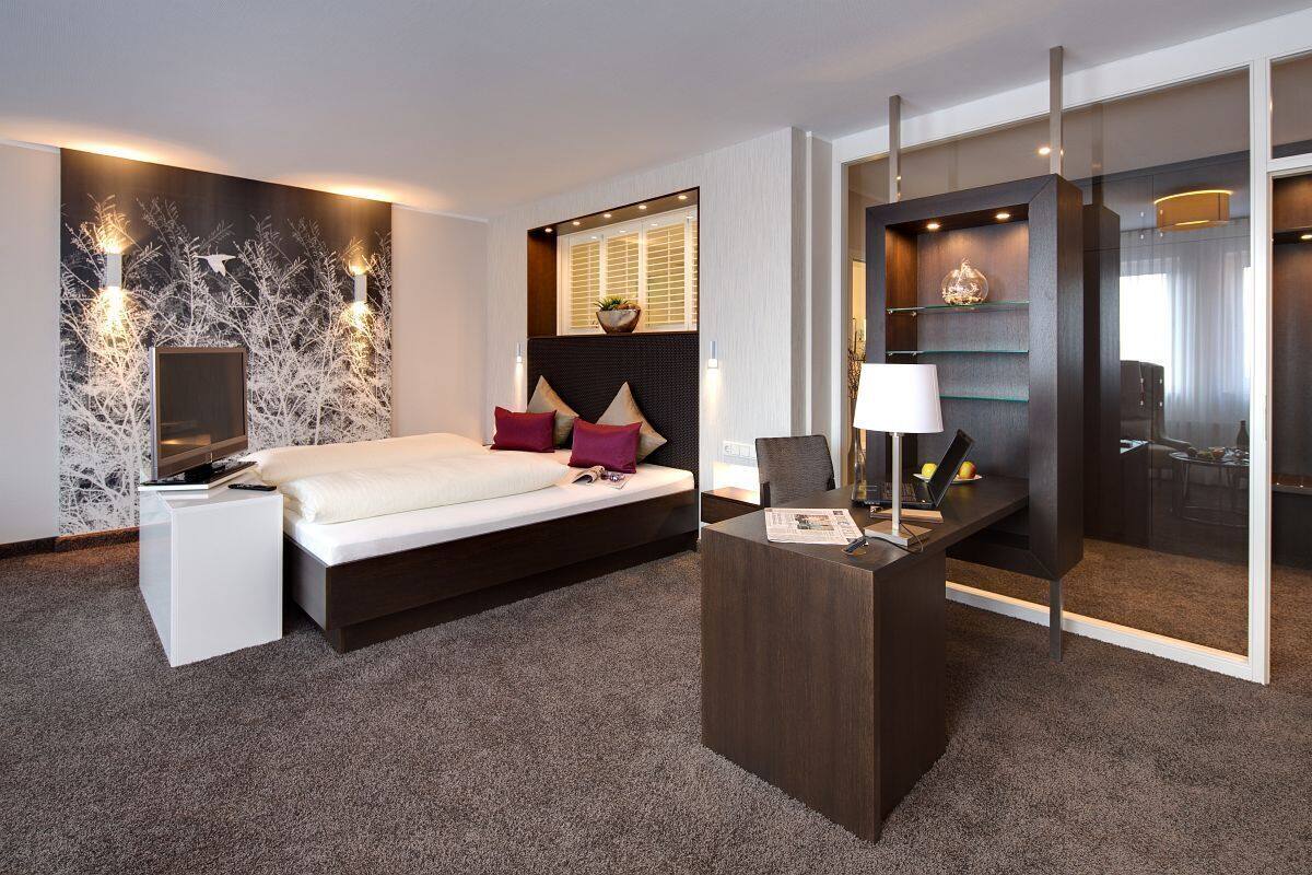 Quarto de hotel moderno com cama, mesa de cabeceira e escrivaninha com abajur.