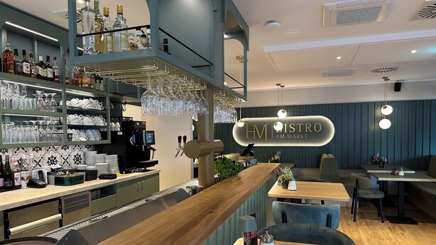 Un moderno bar con una máquina de café, estantes llenos de botellas de licor y vasos ordenados.