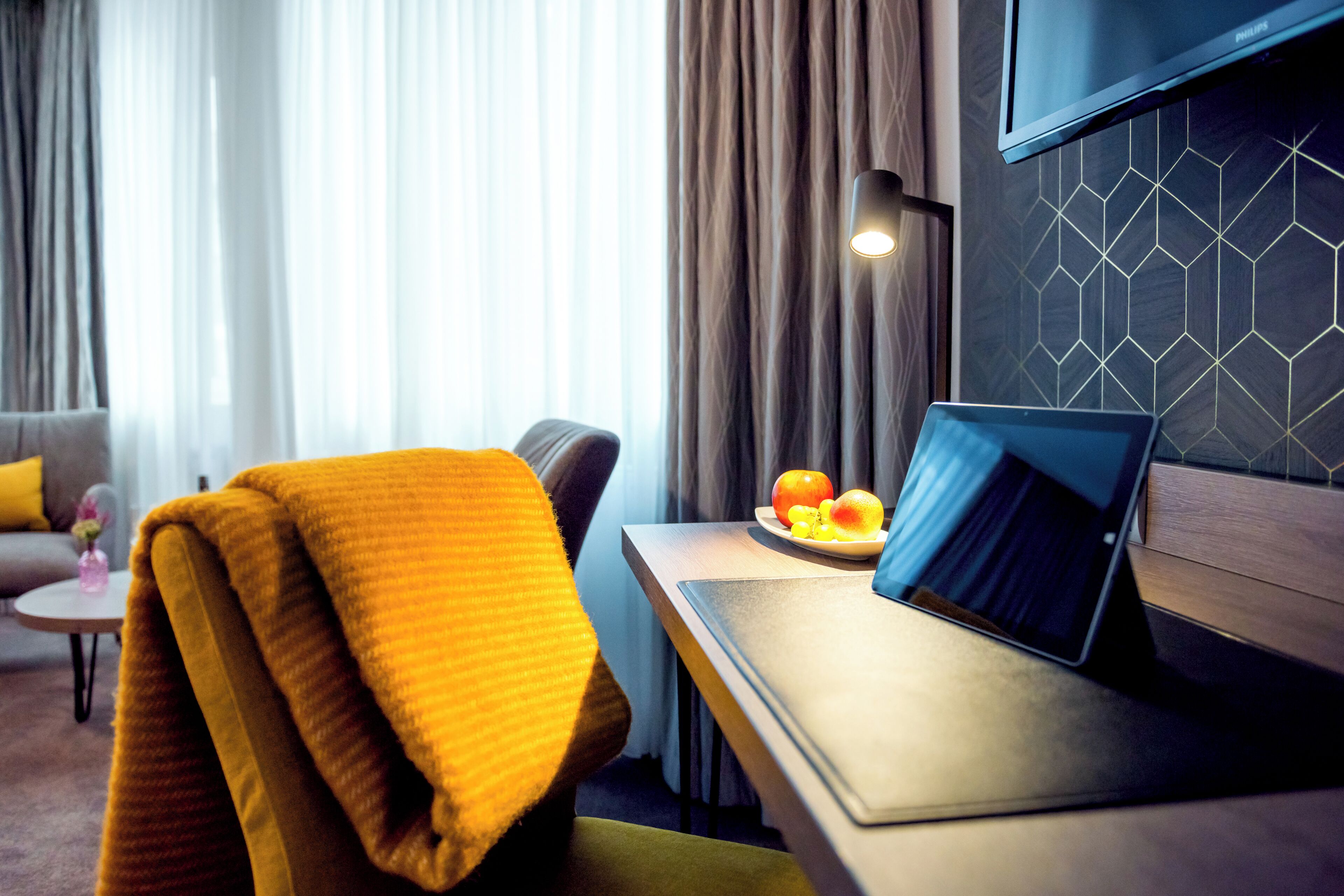 Une chambre d’hôtel moderne avec un bureau en bois, un ordinateur portable et une assiette de fruits.