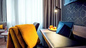 Une chambre d’hôtel moderne avec un bureau en bois, un ordinateur portable et une assiette de fruits.