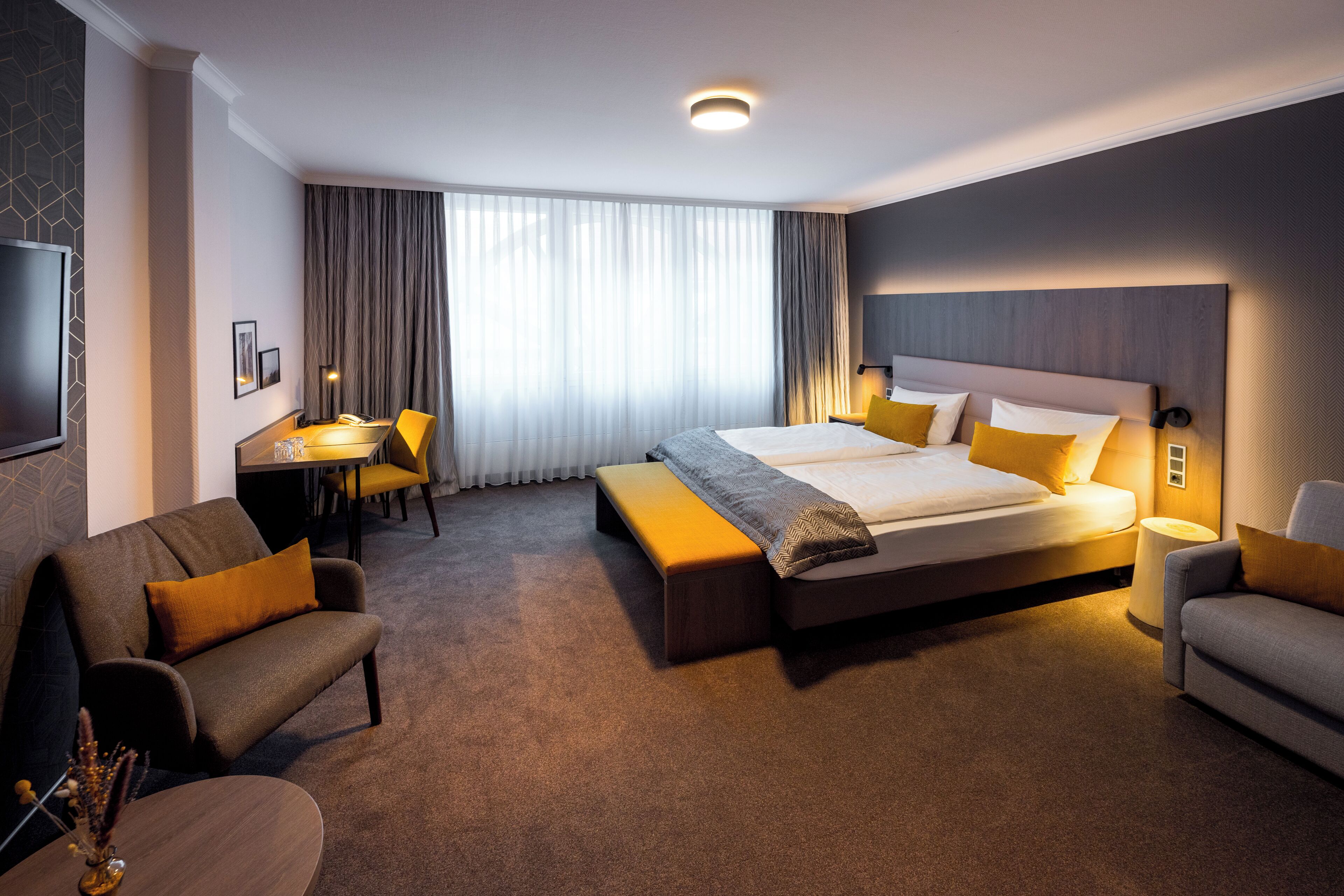 Ein modernes Hotelzimmer mit einem großen Bett, einem Schreibtisch, einer Couch und einem Fernseher.