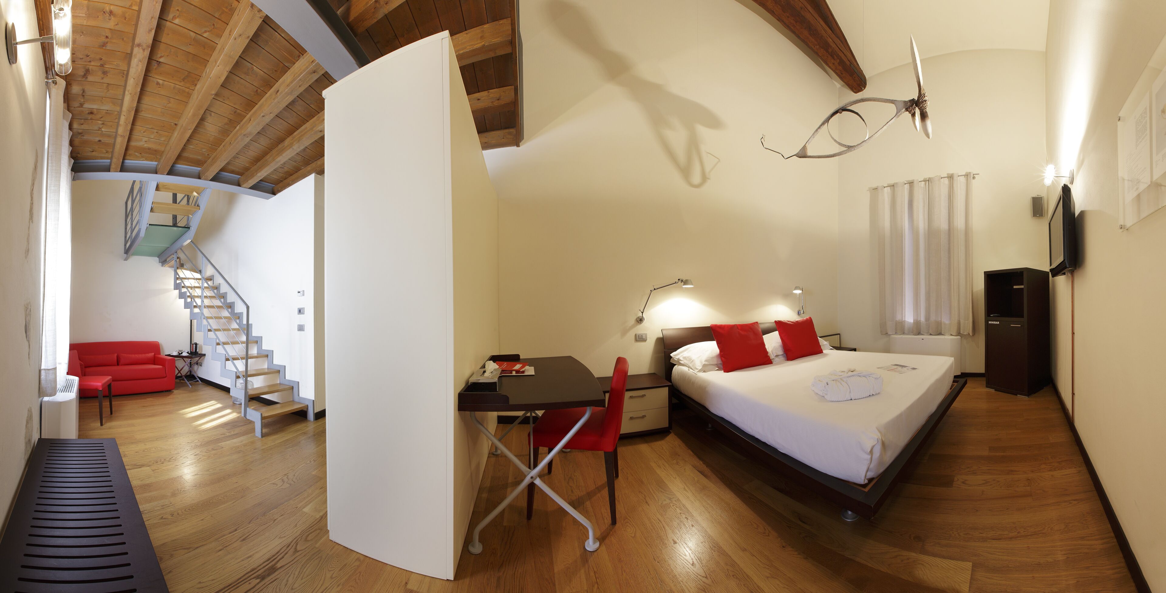 Un dormitorio con cama, escritorio, silla y una escalera que sube a un nivel superior.