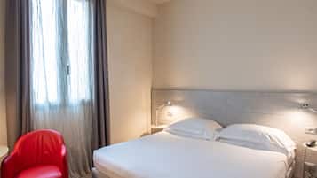 A hotel room with a bed, a red chair, a nightstand, and a window with curtains.