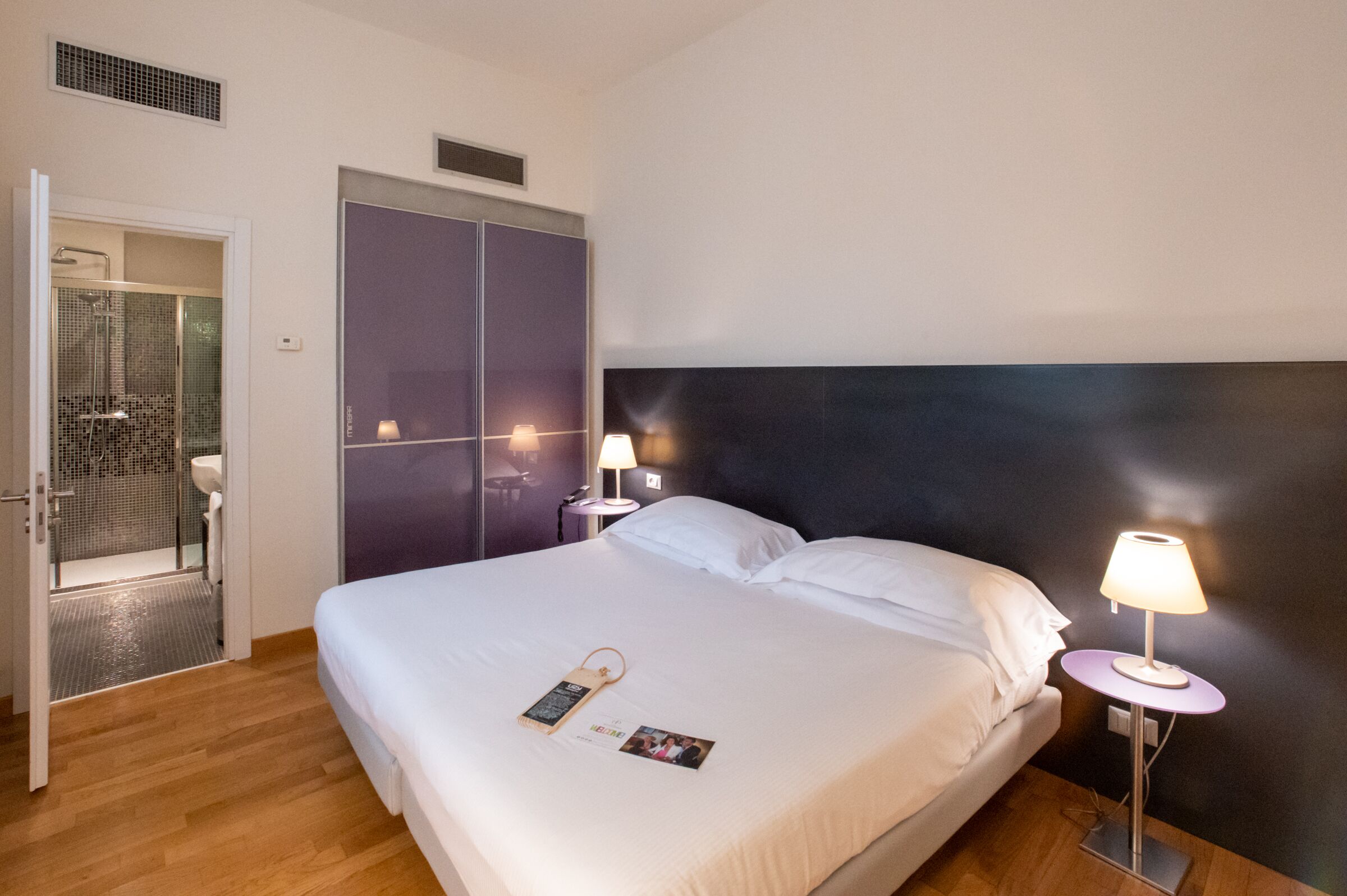 Een hotelkamer met een groot bed, twee bedlampen, een kledingkast en een douche.
