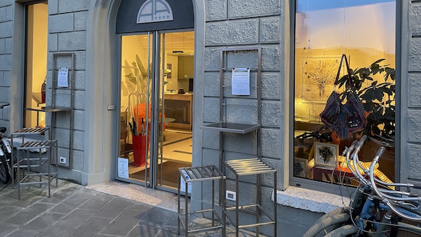 Un edificio con fachada de piedra, puerta de entrada de vidrio y un interior visible con zona de comedor.