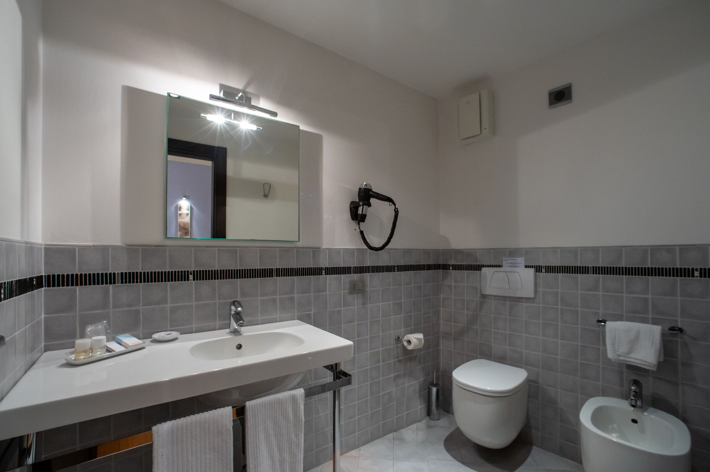 A modern bathroom with a large mirror, two sinks, a toilet, and a bidet.