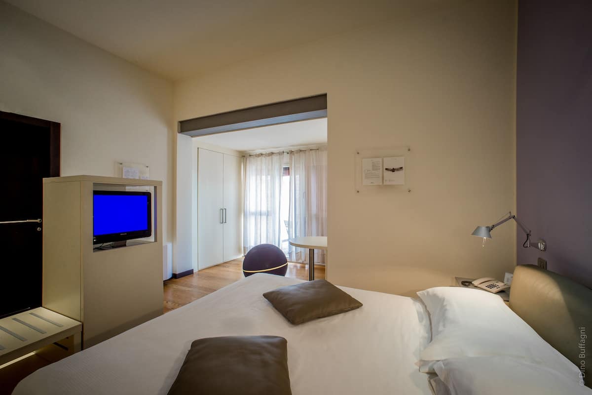 A hotel room with a bed, a desk with a computer, a chair, a desk lamp, and a telephone.