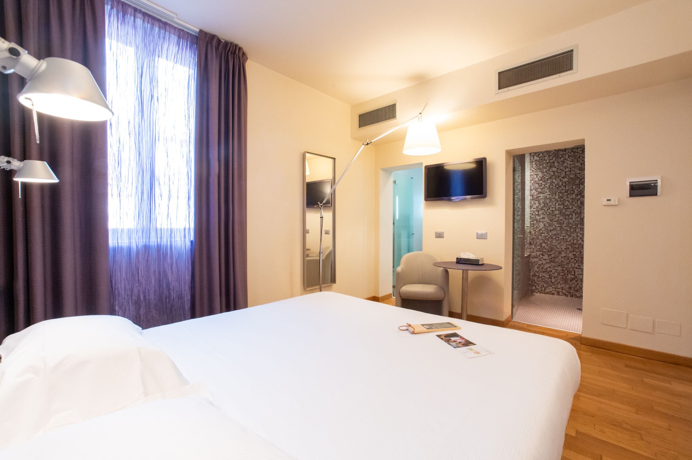 Une chambre d’hôtel avec un grand lit, un bureau, une chaise, une télévision et un espace douche.