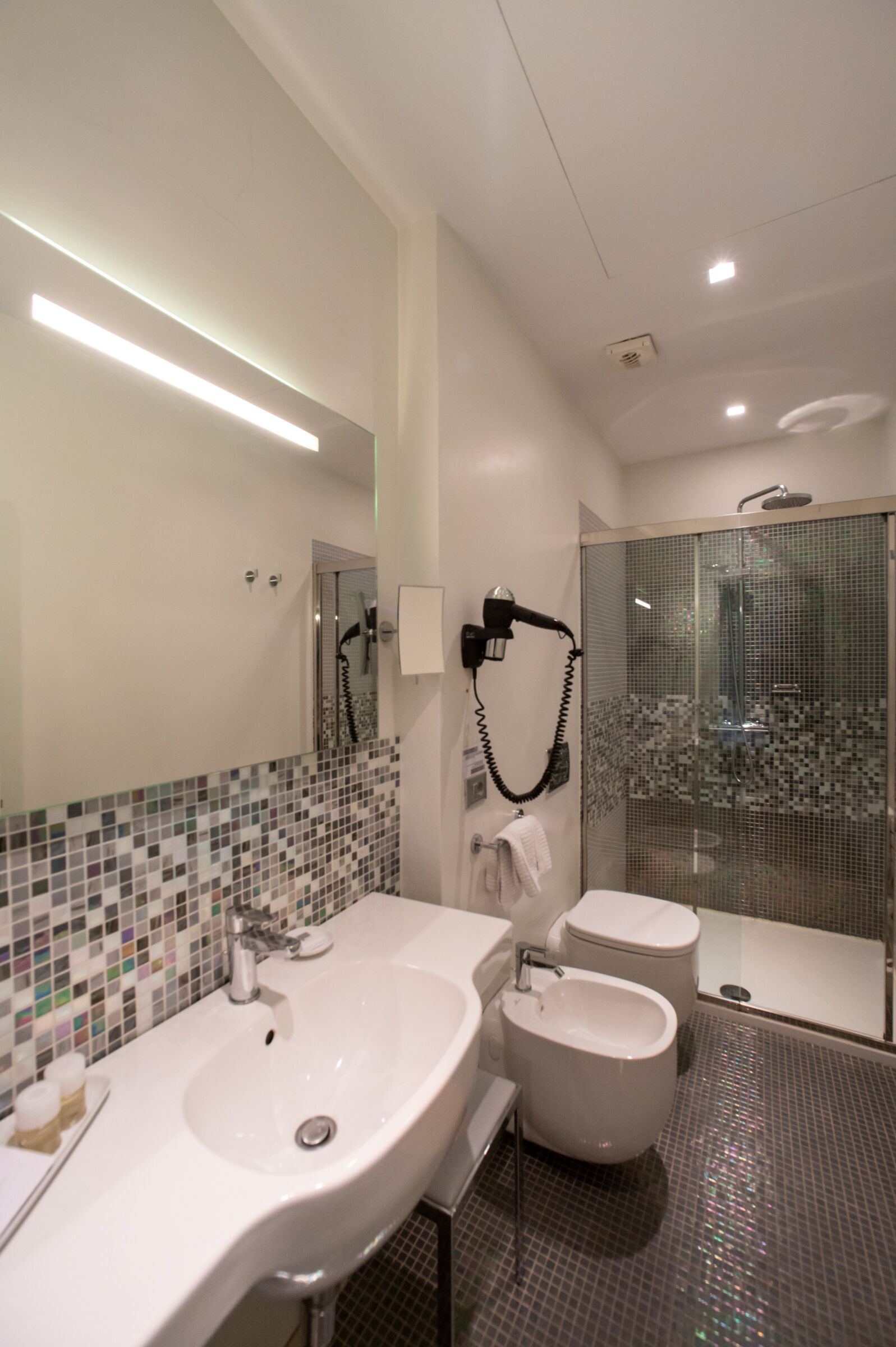 Un baño moderno con un espejo grande, dos lavamanos, un bidé y una ducha con mampara de vidrio.