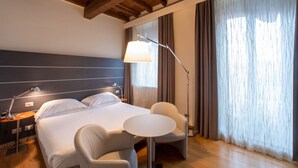 Una habitación de hotel con cama, mesita de noche, lámpara, silla y una pequeña mesa.