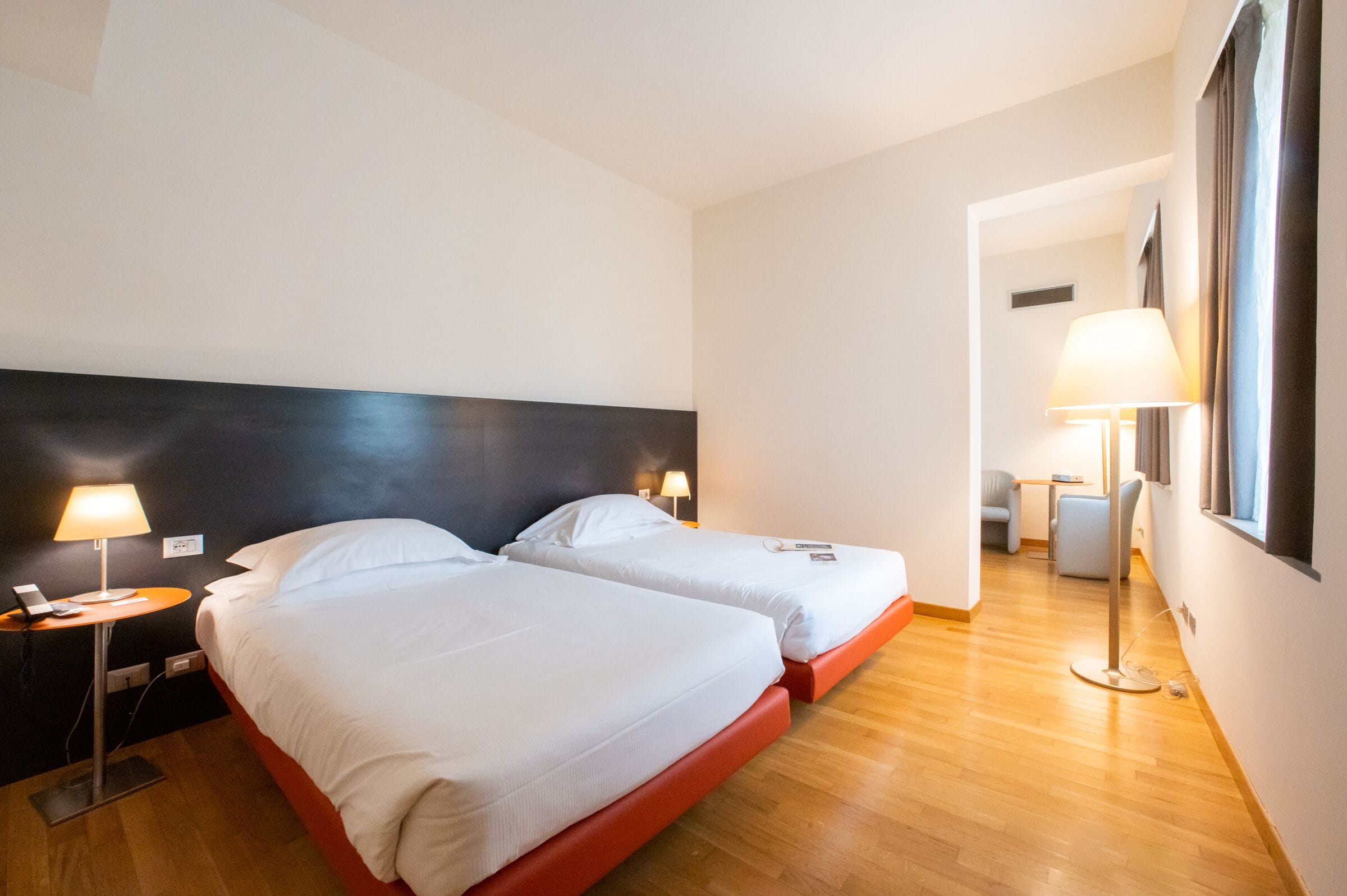 Habitación de hotel con dos camas, un escritorio, una silla y una lámpara.