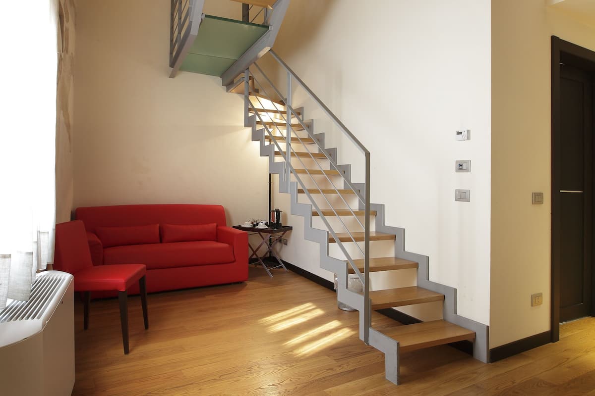 A modern living room with a wooden floor, a red sofa, a staircase, and a black door.