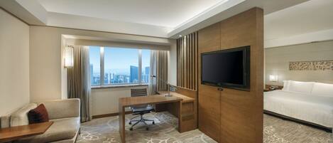 Une chambre d’hôtel dotée d’un grand lit, d’un bureau avec une chaise, d’une télévision et offrant une vue sur le panorama urbain grâce à de grandes fenêtres.