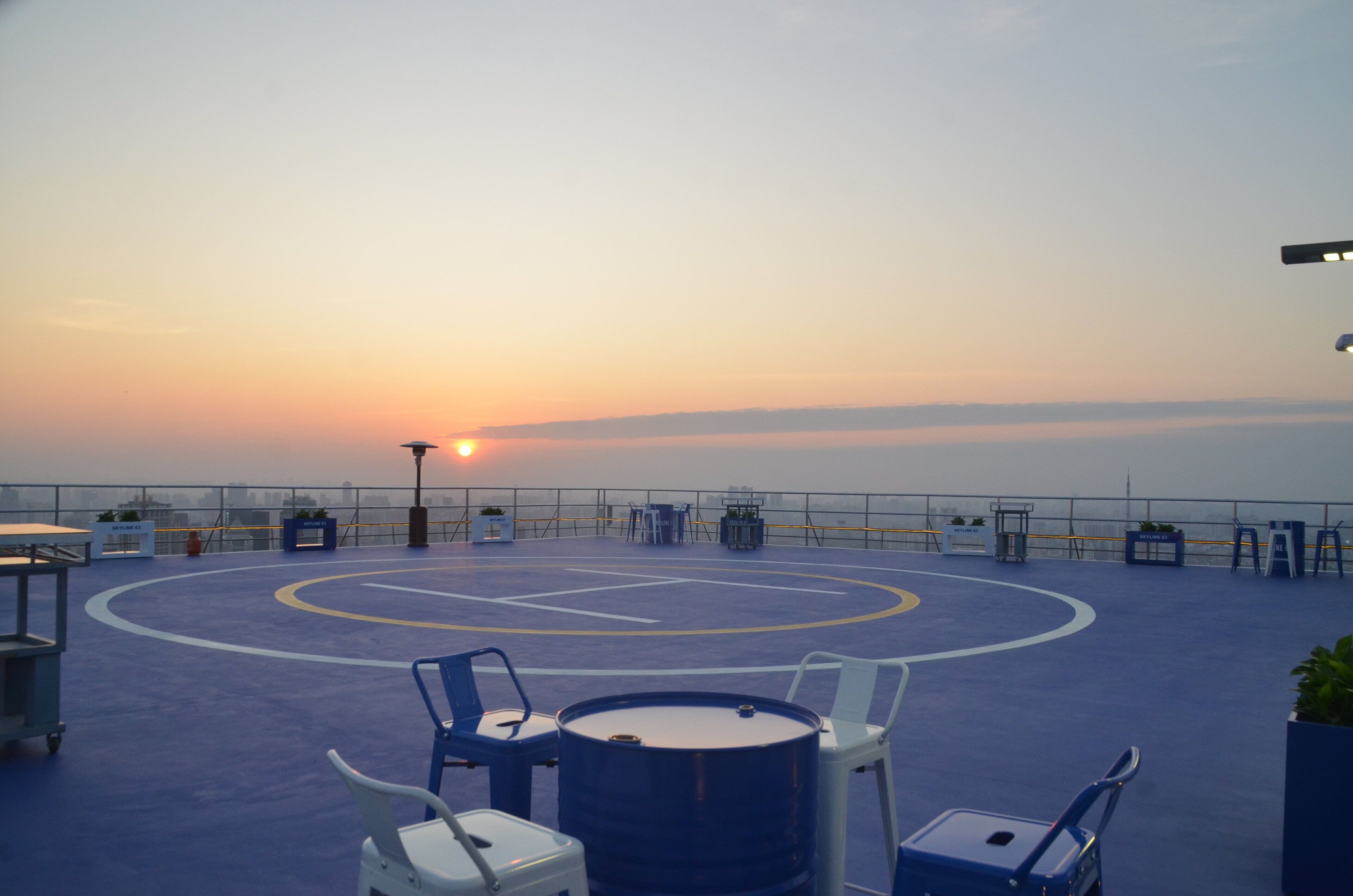 A rooftop terrace with a sunset view, tables, chairs, and a basketball court.