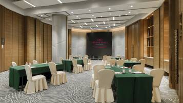 Un salón de conferencias con varias mesas, sillas y una pantalla grande mostrando “CROWNE PLAZA GUANGZHOU CITY CENTRE”.