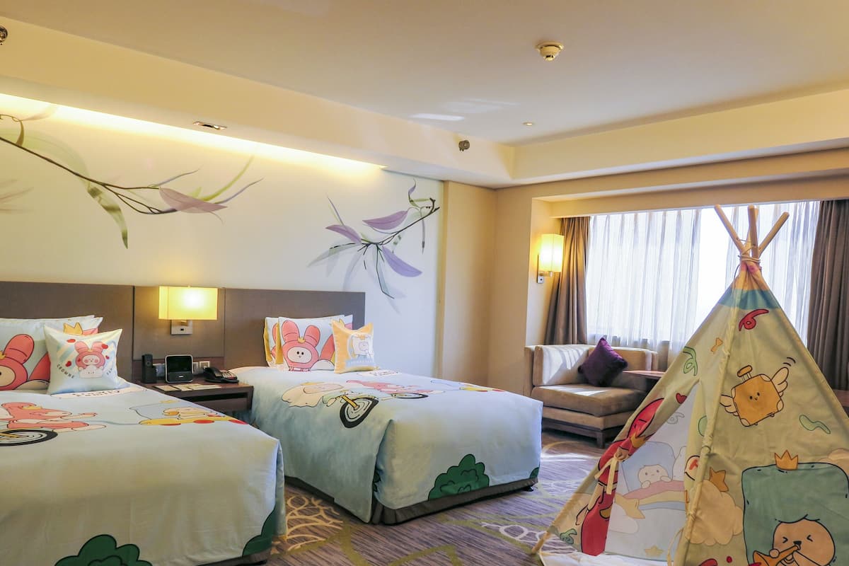 A hotel room with two beds, a desk, a chair, a lamp, a window with curtains, and a teepee.