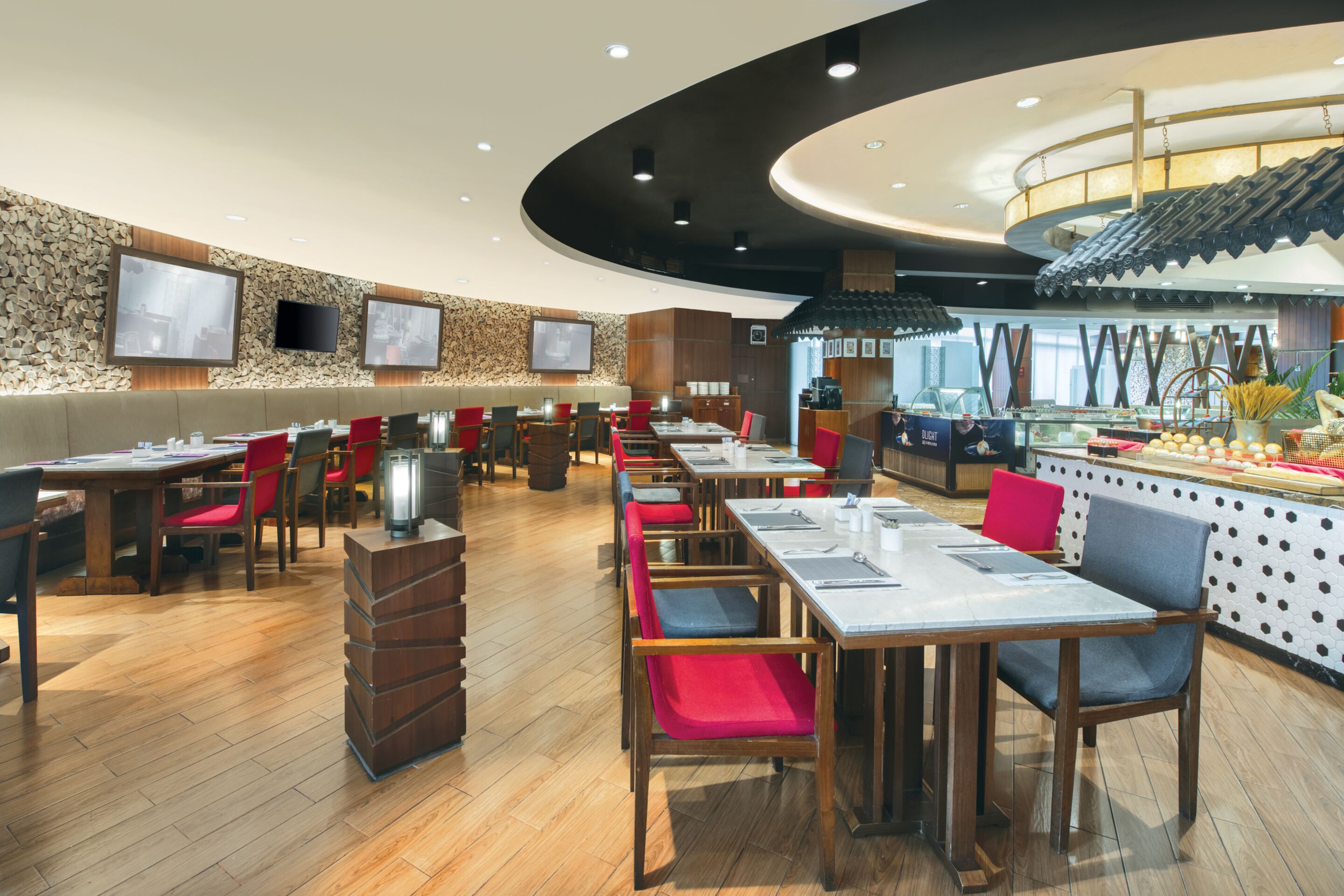 A modern restaurant with wooden flooring, red and grey chairs, and a central bar area.