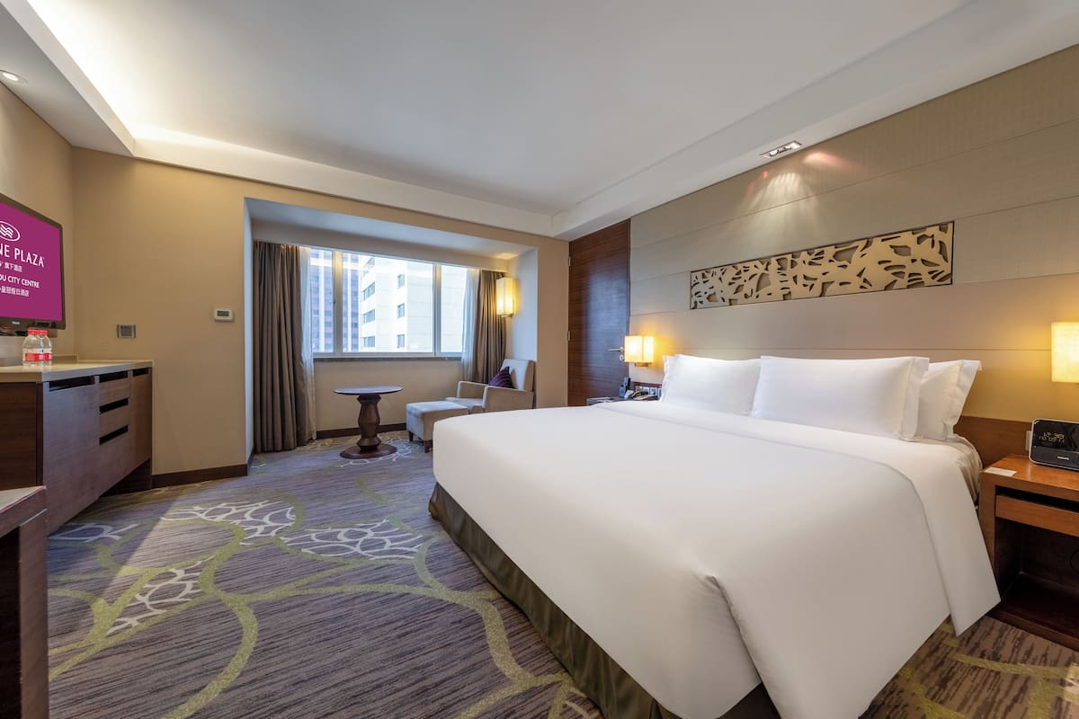 A hotel room with a large bed, a desk, a chair, a small table, and a window with curtains.