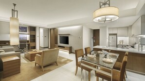 A modern hotel room with a dining area, a TV, and a kitchenette.